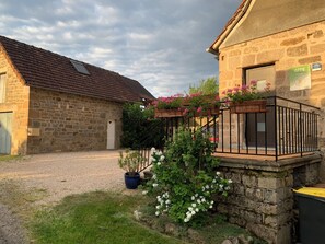 Un edificio de piedra con camino de grava, una escalera de madera y macetas con plantas.