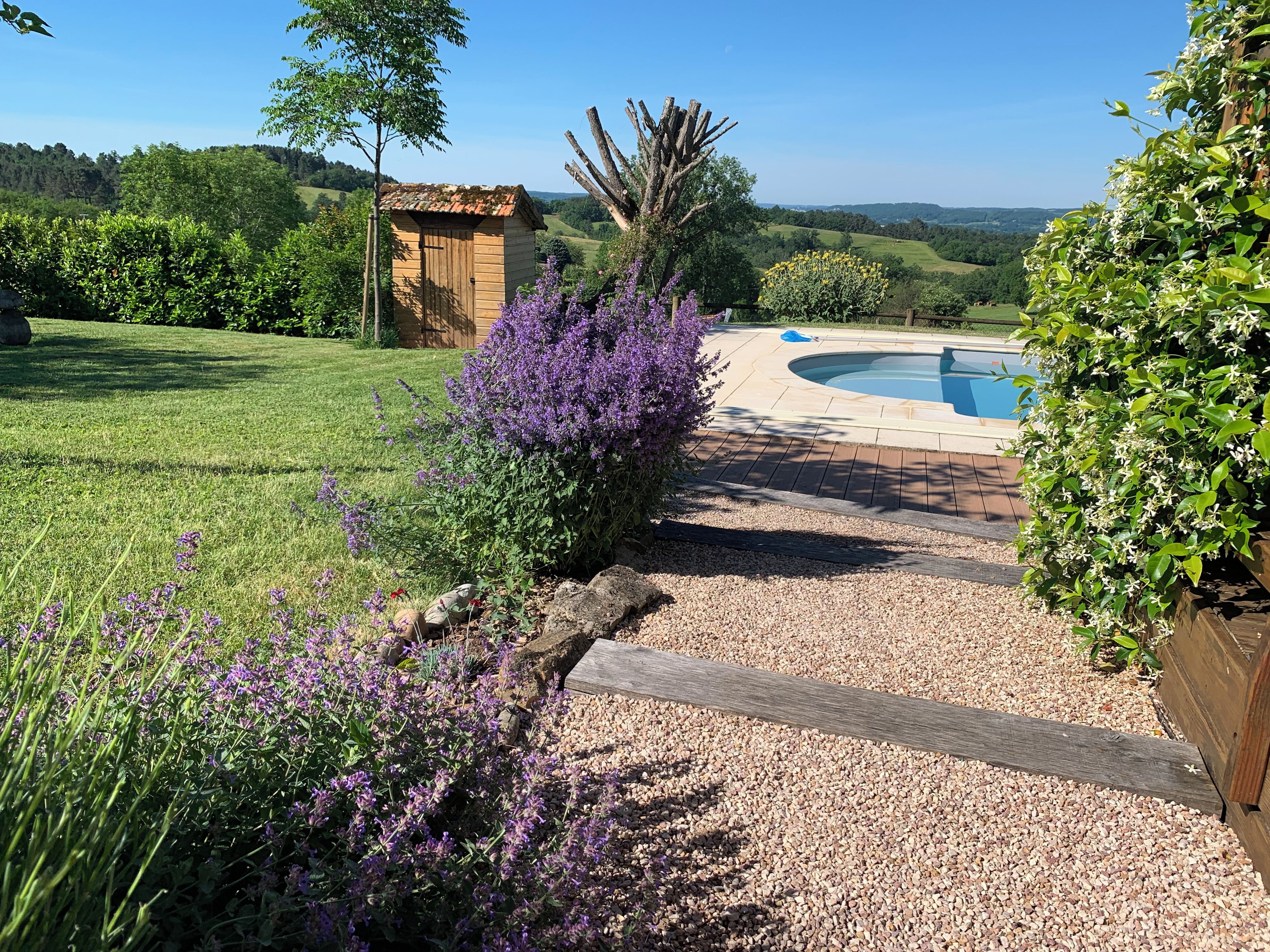 Zona de piscina con terraza de madera, rodeada de grava y vistas al campo.