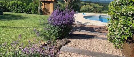 Zona de piscina con terraza de madera, rodeada de grava y vistas al campo.