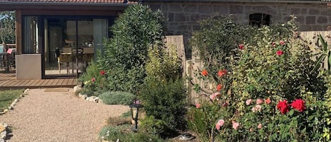 A stone house with a tiled roof, a gravel driveway, and a garden with flowers.