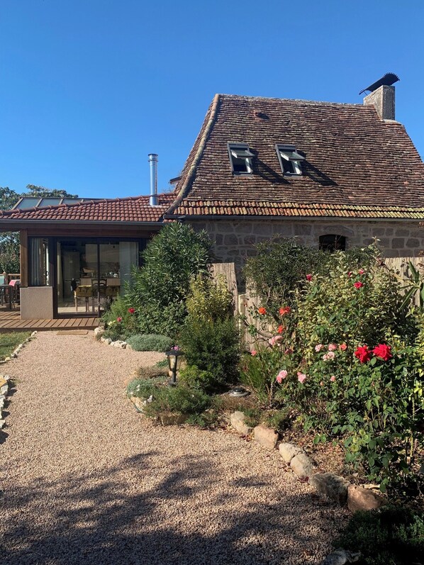 A stone house with a tiled roof, a gravel driveway, and a garden with flowers. - Maison de Charme**** with swimming pool and spectacular view (Curemonte)