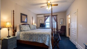 A bedroom with a four-poster bed, a nightstand with a lamp, a chair, and a view of the outdoors through a window. - Find genuine southern hospitality in Hendersonville at the 1898 Waverly Inn. (Hendersonville)