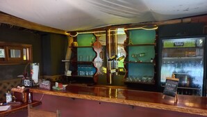 Zona de bar con mostrador de madera, estanterías con vasos y un menú en la pizarra.
