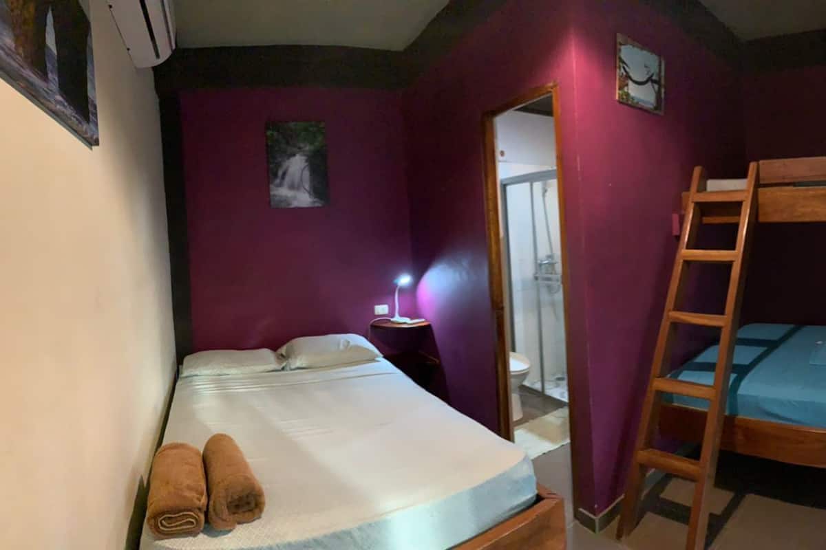 Una habitació amb un llit doble i un llit senzill, amb roba de llit blanca a ambdós. Hi ha una escala de fusta adossada al llit doble.