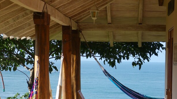 Un porche de madera con una hamaca, una silla de madera y vista al mar.