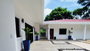 Un pasillo con plantas en macetas, piso de baldosas y un edificio con techo rojo.