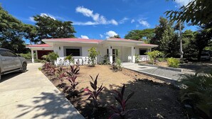Una casa de dos pisos con techo rojo, camino de entrada y jardín con diversas plantas.