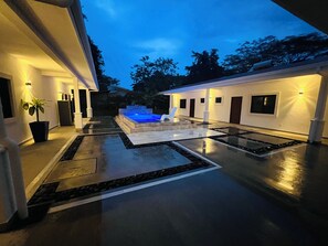 A modern house with a swimming pool, a well-lit patio, and a stone pathway.