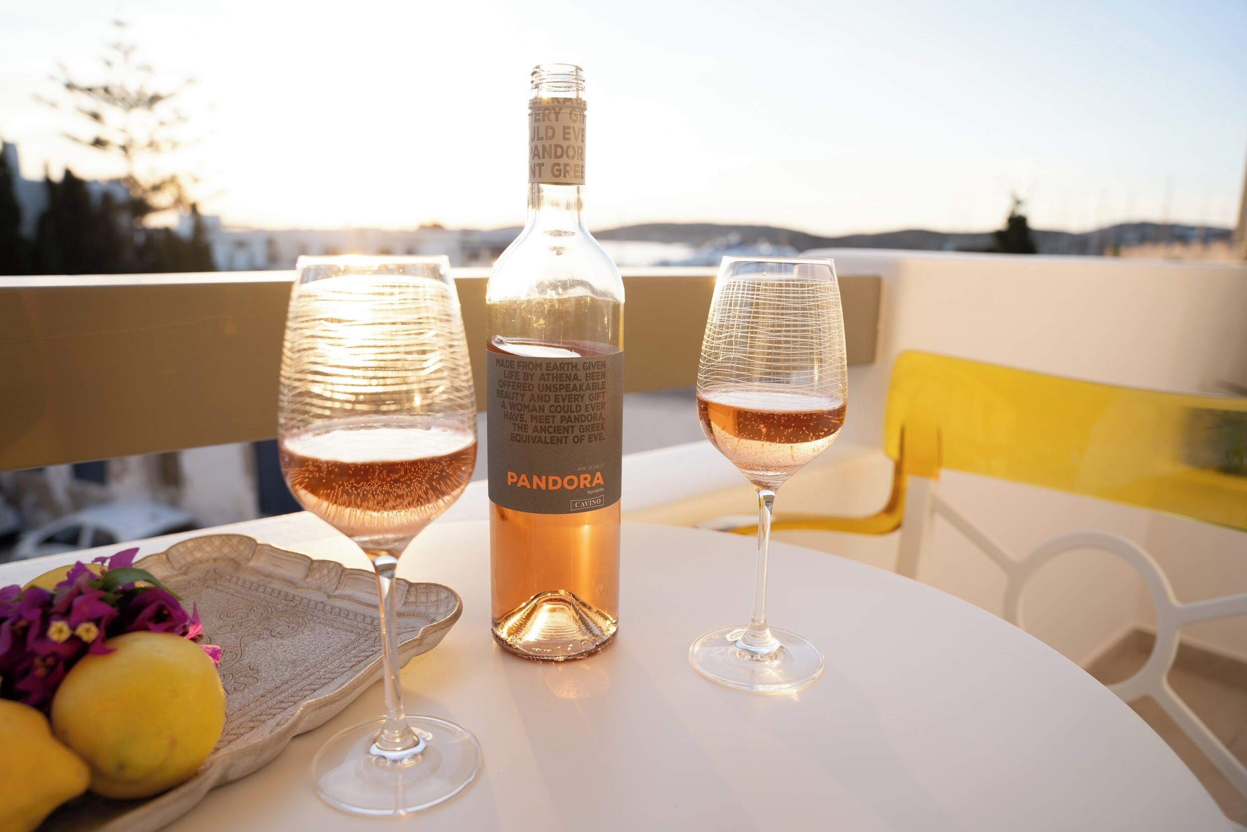 A table with two glasses of wine, a bottle of wine, and a tray with lemons and flowers.