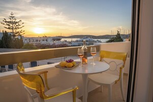 A balcony with a table set for two, featuring a bottle and glasses, and a plate of lemons and flowers.