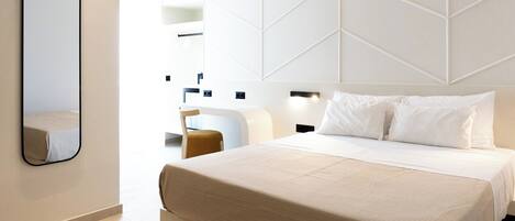 A modern hotel room with a large bed, a bedside table, a chair, and a mirror.