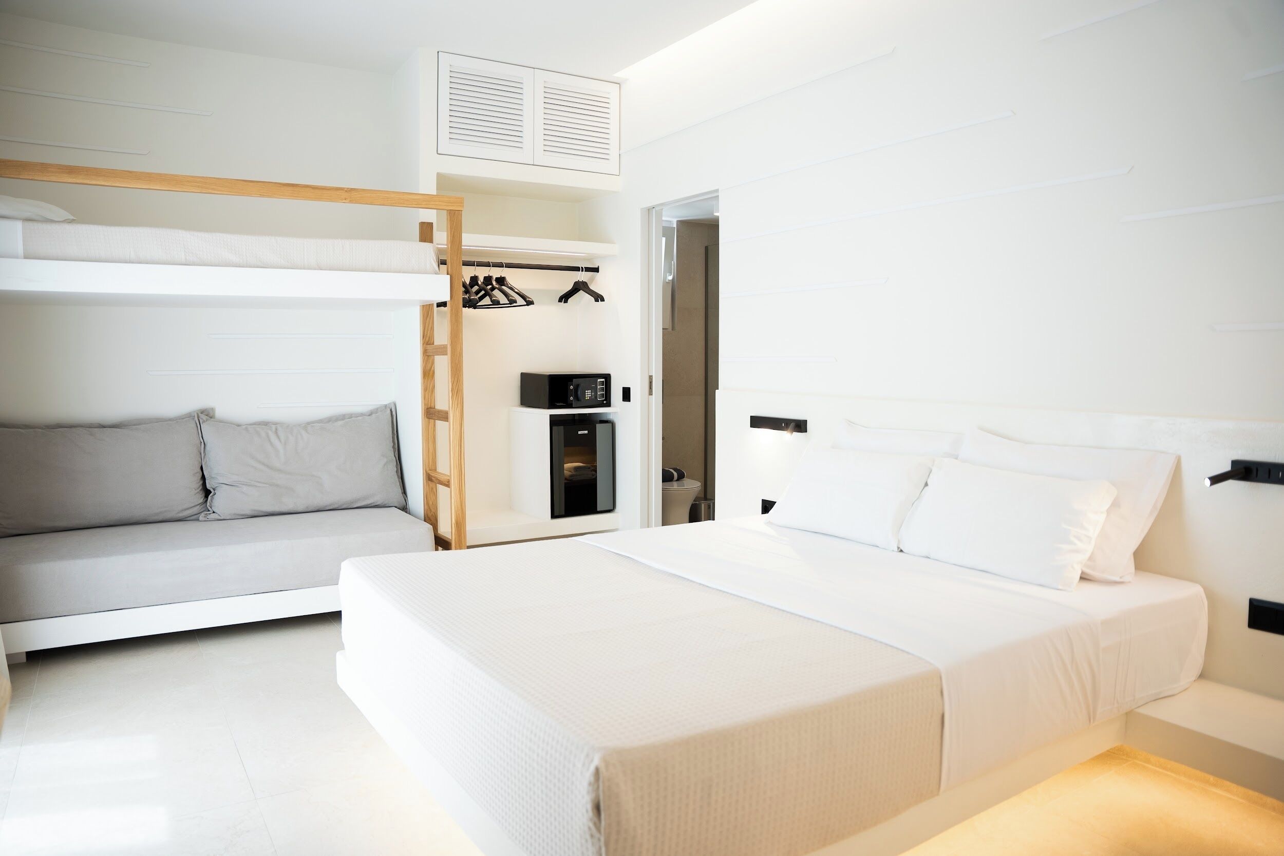 Quarto moderno com cama beliche, cama de solteiro, guarda-roupa e uma pequena cozinha compacta.