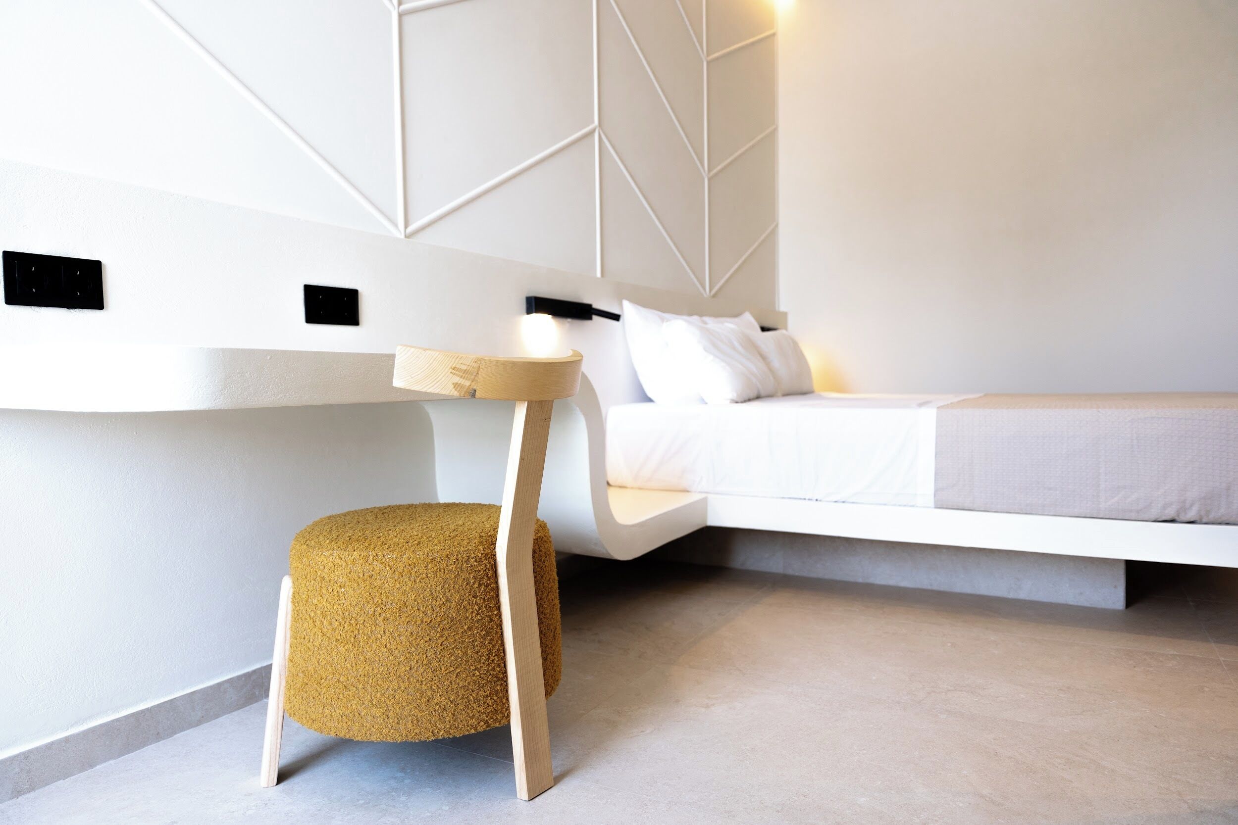 A modern bedroom with a built-in bed, a small round stool, and a bedside table with a lamp.