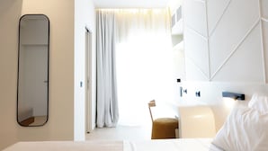 Een hotelkamer met een groot bed, een nachtkastje, een stoel, een spiegel en een raam met gordijnen.
