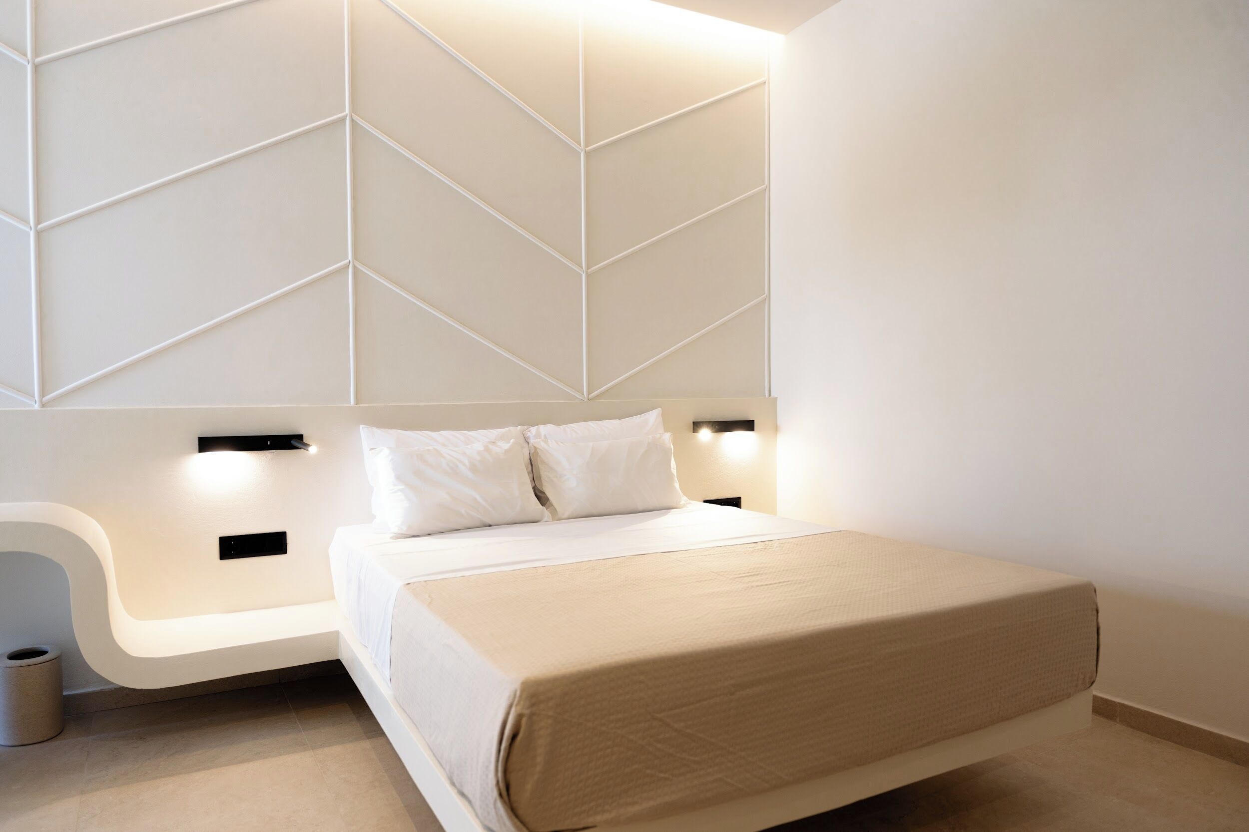 A modern bedroom with a bed, bedside tables, and a geometric wall design.