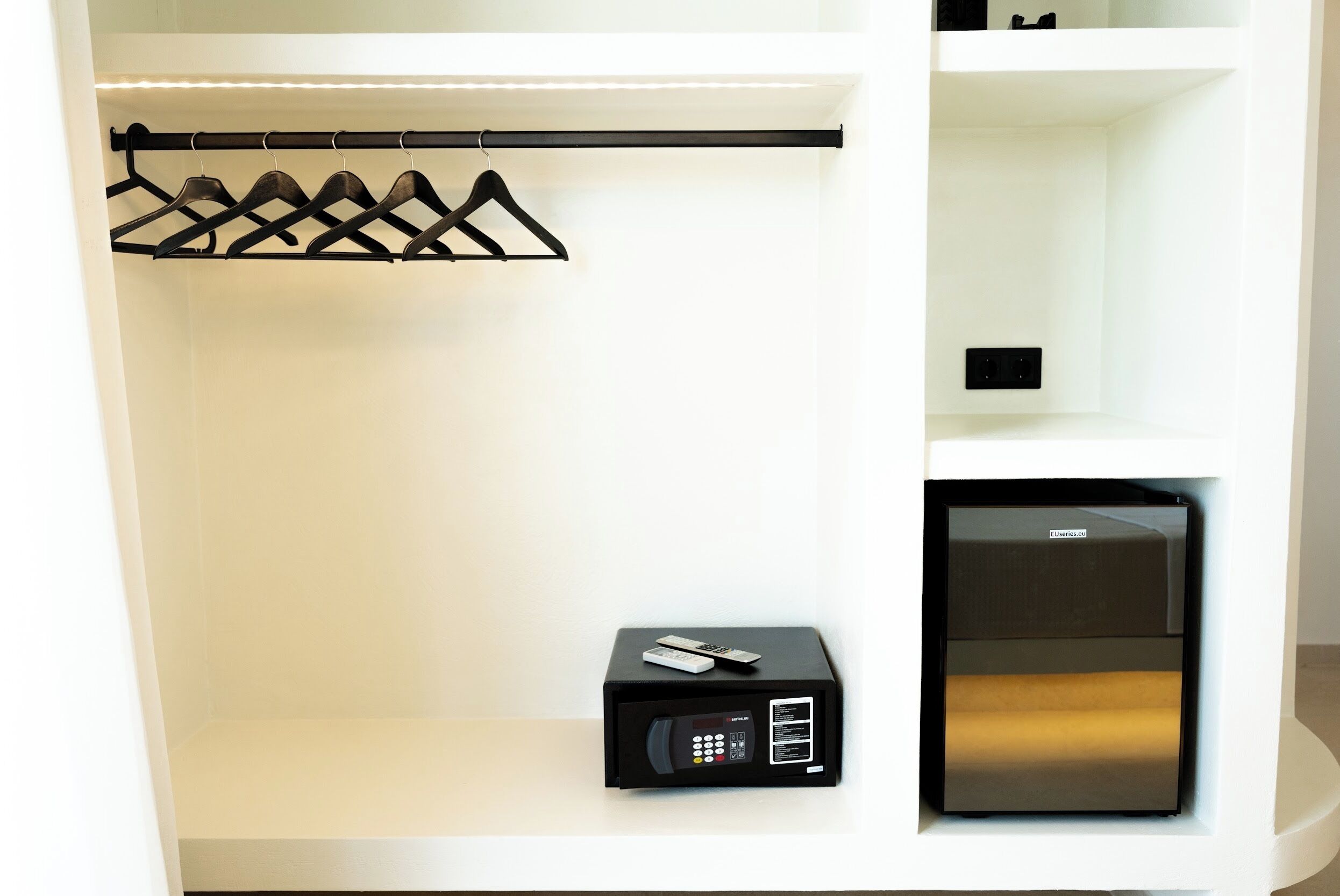A white closet with a black hanging organizer, a black electronic device, and a black appliance.
