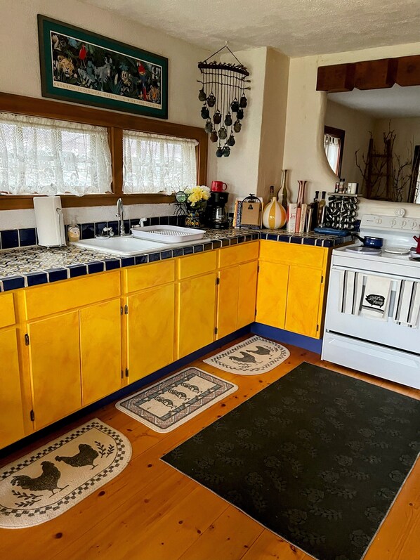 Una cocina con gabinetes amarillos, una estufa blanca y una ventana con cortinas de encaje.