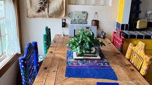 A dining area with a wooden table, blue chairs, a decorative wreath, and a wall-mounted light fixture. - Mountain getaway in the heart of La Veta! (La Veta)