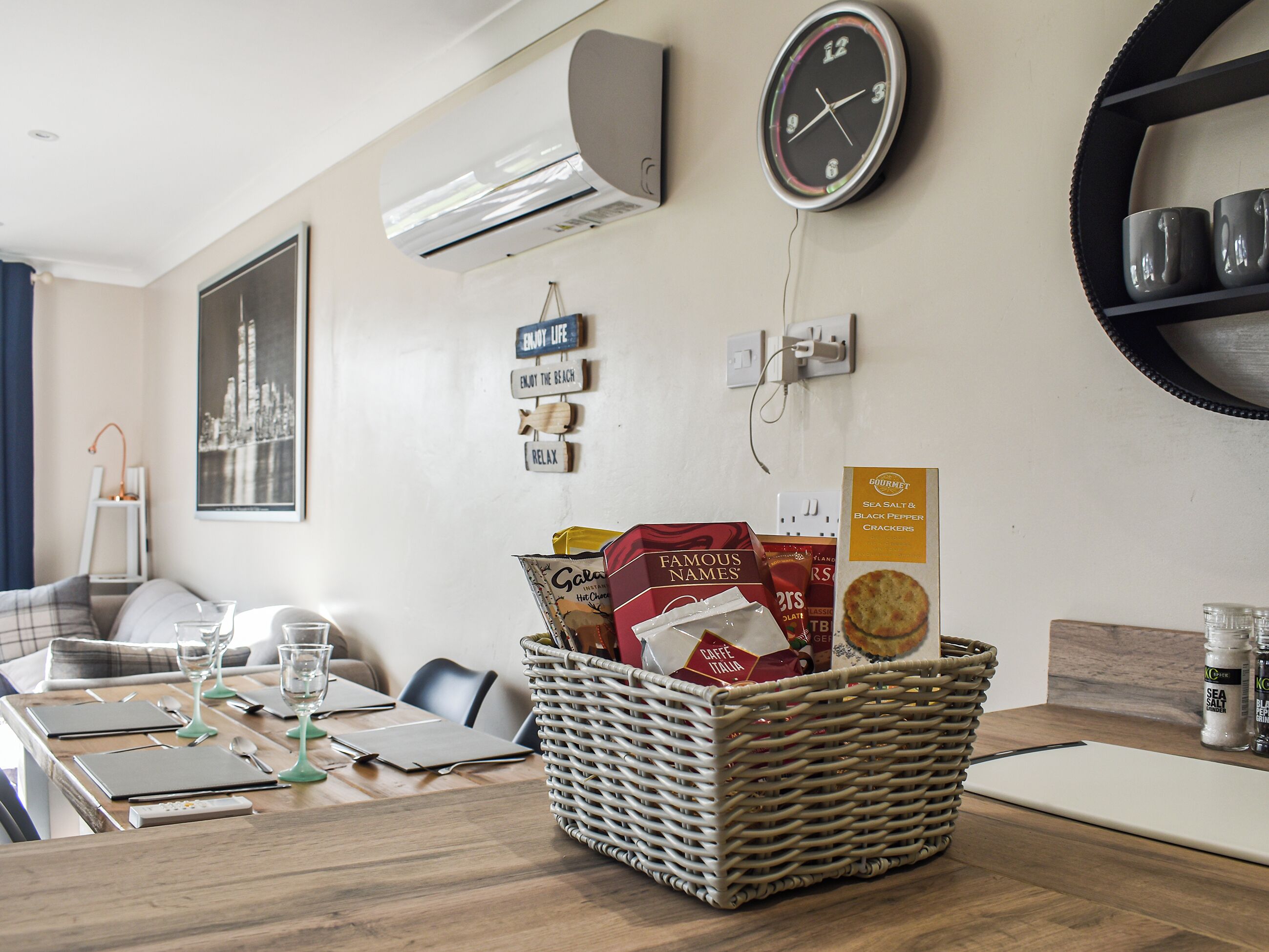Ein Essbereich mit Tisch für zwei Personen, einem Korbwäscher mit Snacks, einer Uhr und Wanddekorationen.