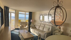 A hotel room with a balcony, a sofa, a dining table, and a chandelier. - Spacious Oceanfront 2-bedroom Condo in Bay Watch in beautiful North Myrtle Beach (North Myrtle Beach)