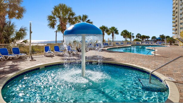 A pool area with a water fountain, lounge chairs, and palm trees. - Spacious Oceanfront 2-bedroom Condo in Bay Watch in beautiful North Myrtle Beach (North Myrtle Beach)