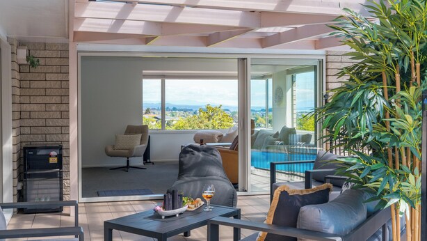 A modern outdoor living area with a sofa, table, and chairs, a glass door leading to a pool, and a view of the cityscape.