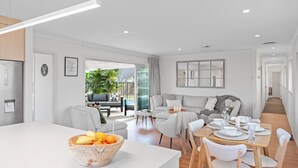 A modern living room with a dining area, featuring a large window, a sofa set, and a fruit bowl on the dining table.