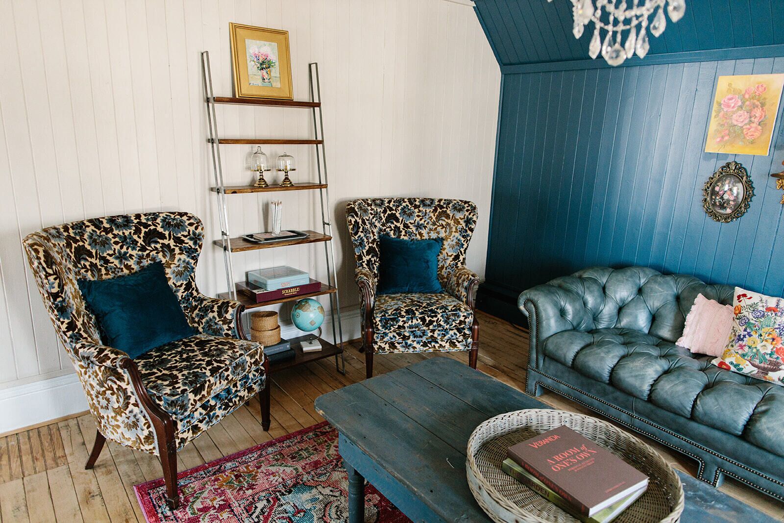 A living room with two patterned armchairs, a blue sofa, a wooden coffee table, and a bookshelf with decorative items.