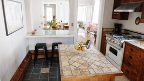 A kitchen with a tiled island, two bar stools, a stove, and wooden cabinets.
