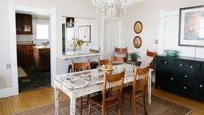 A dining area with a white table, wooden chairs, a chandelier, and a dark-colored cabinet.