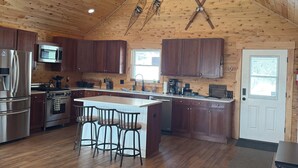 Una cocina amplia con armarios de madera, una isla central con taburetes de bar, un ventilador de techo y un ventanal grande.