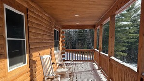 Una cabaña de madera con un porche cubierto, mecedoras y vistas a un bosque.