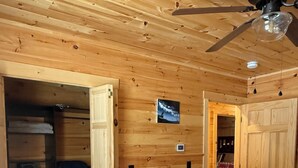 Un dormitorio de cabaña de madera con cama, ventilador de techo y armario.