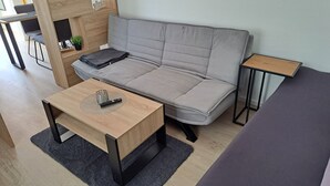 Un salon moderne avec un canapé gris, une table basse en bois avec une télécommande, une petite table d’appoint et un tapis gris.