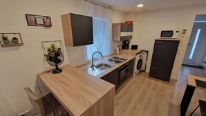 Une cuisine de taille réduite équipée d’un évier, d’une cuisinière, d’un four à micro-ondes et d’un lave-linge.