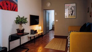 A modern living room with a flat-screen TV, a potted plant, a yellow sofa, and a framed poster. - Navona Boutique Apartment with terrace (Rome)