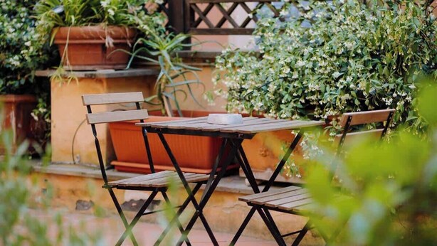 An outdoor patio with a wooden table and chairs, surrounded by potted plants and a lattice fence. - Navona Boutique Apartment with terrace (Rome)