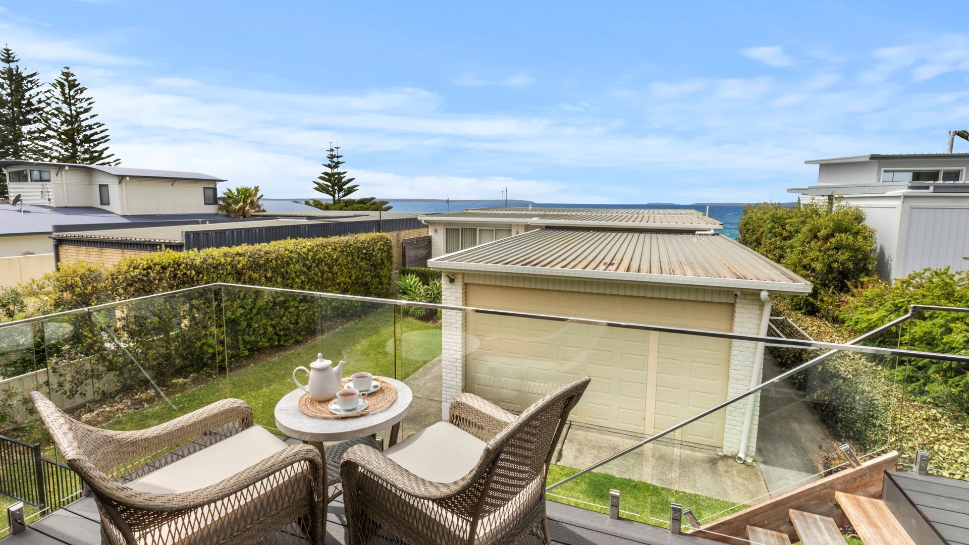 A balcony with wicker furniture and a table set for two, overlooking a residential area and a body of water.