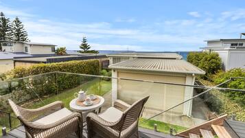 A balcony with wicker furniture and a table set for two, overlooking a residential area and a body of water.