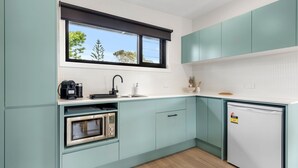 A modern kitchen with teal cabinets, a built-in oven, a dishwasher, and a window with a view of trees. - Azure Studio - Ocean Glimpses - 3 Mins Walk to Beach (Callala Beach)