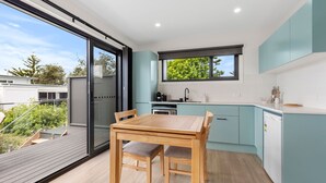 A modern kitchen with a dining area, large windows, and a view of the outdoors. - Azure Studio - Ocean Glimpses - 3 Mins Walk to Beach (Callala Beach)