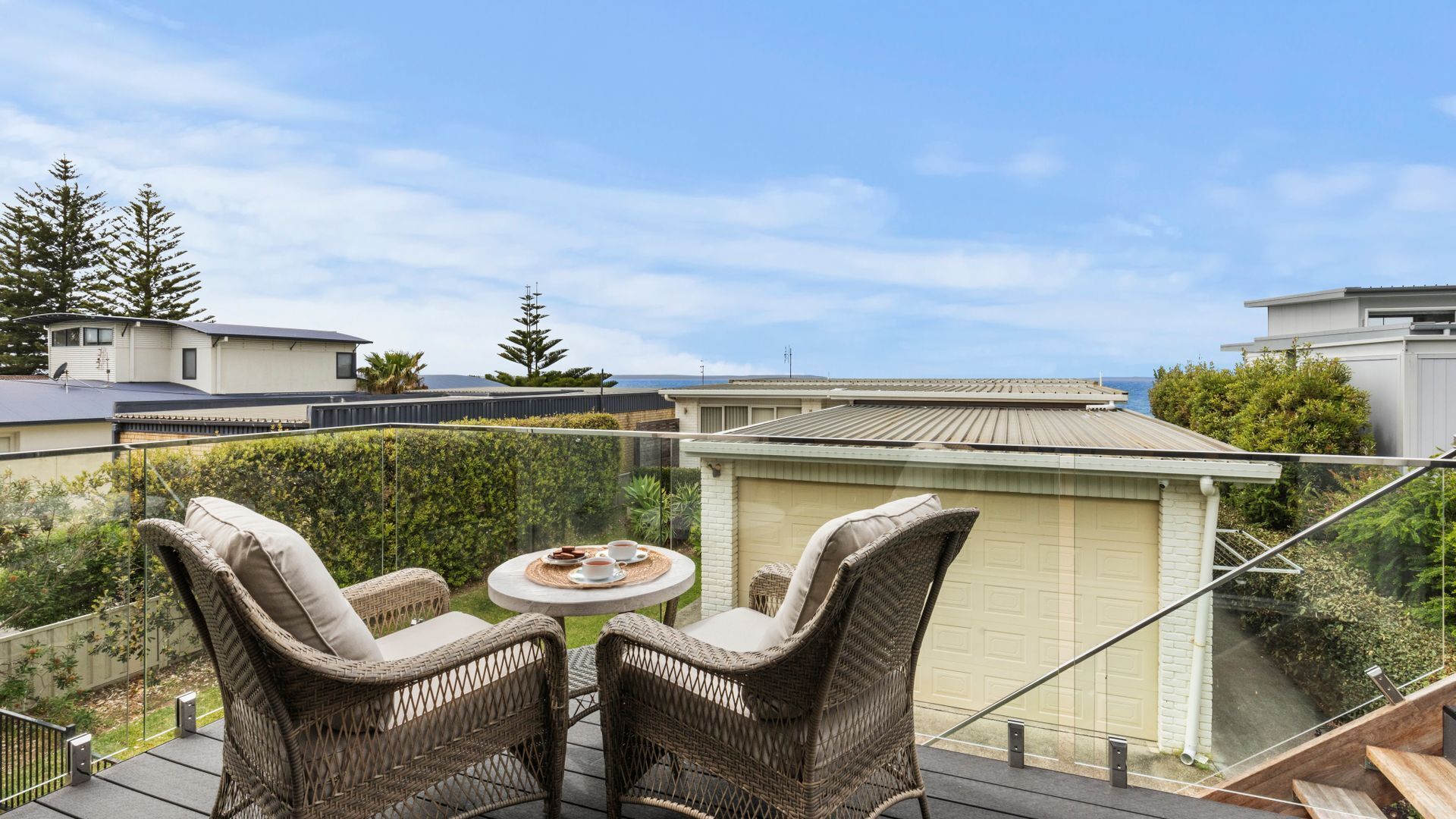 A balcony with wicker furniture and a table, overlooking a residential area with houses and a clear sky.