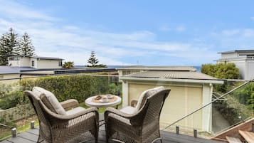 A balcony with wicker furniture and a table, overlooking a residential area with houses and a clear sky.
