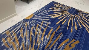 A modern living room with a large blue and gold patterned rug, two white armchairs, a wooden wardrobe, and a flat-screen TV mounted on the wall. - XYZ Hotel - King Fahd Road (Riyadh)