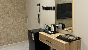 A modern bathroom with a wooden vanity, a large mirror, a black refrigerator, and a red ottoman. - XYZ Hotel - King Fahd Road (Riyadh)