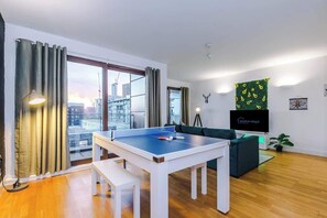 Una sala de estar moderna con una mesa de ping pong, un sofá, un televisor y vistas a la ciudad.