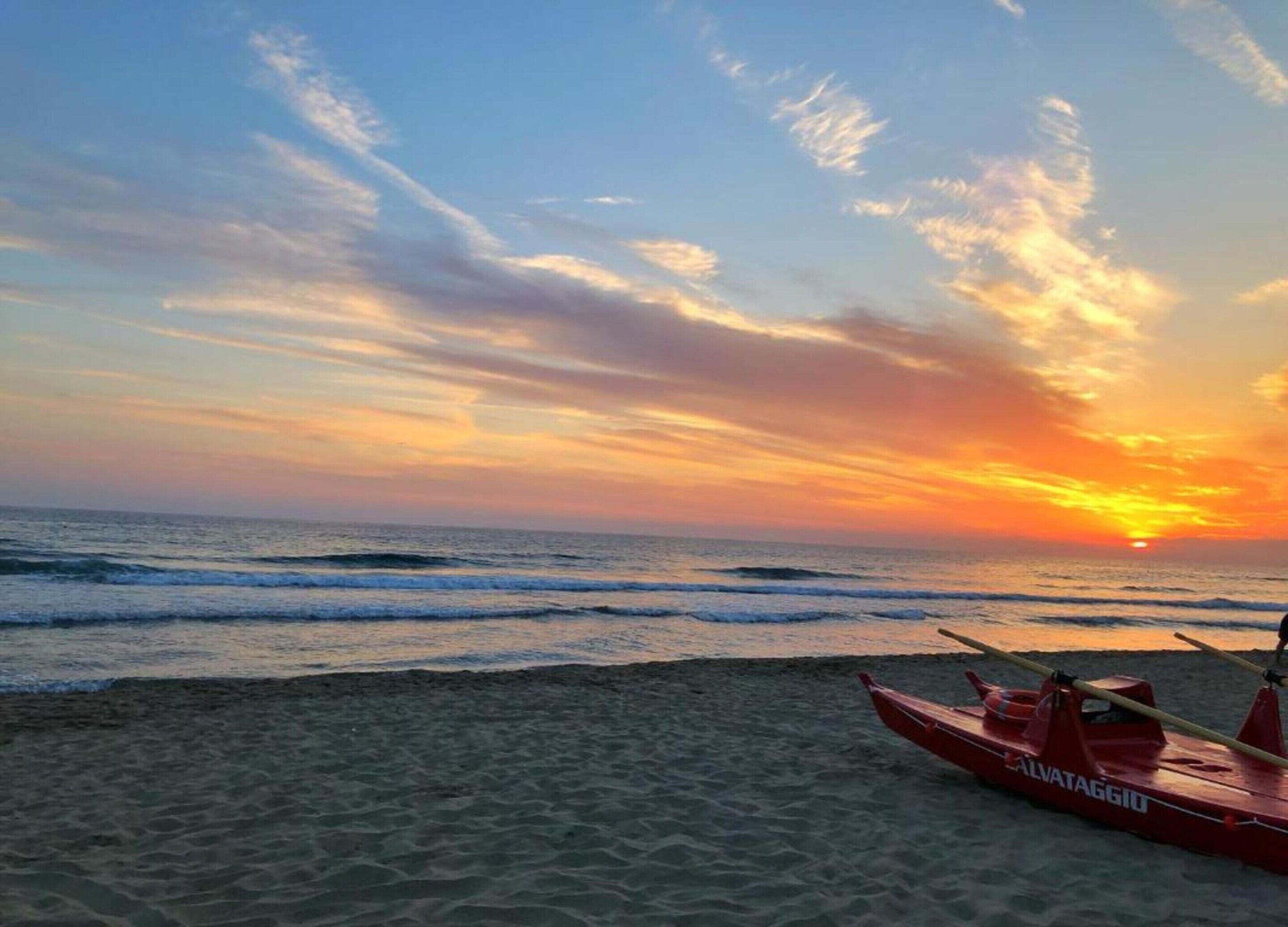 Ein Sonnenuntergang über dem Meer mit einem roten Rettungsboot mit der Aufschrift "ALVATAGGIO" am Strand.