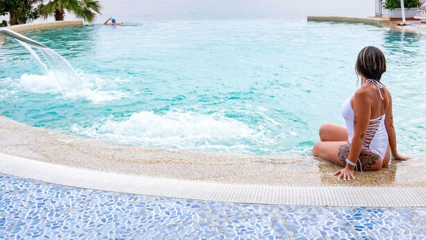 A person sitting by a pool with a clear view of the ocean and palm trees.