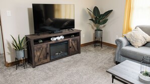 Ein Wohnzimmer mit Fernseher auf einer Holz-Unterhaltungsecke, einem grauen Sofa, einem Couchtisch und einem Topfpflanzen.