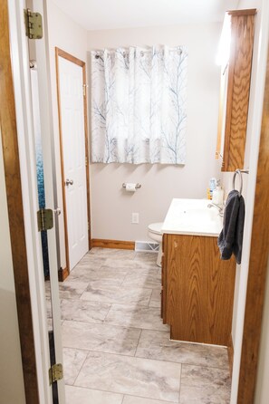 Un baño con lavamanos blanco, armarios de madera, inodoro y cortina de ducha con estampado de árboles.